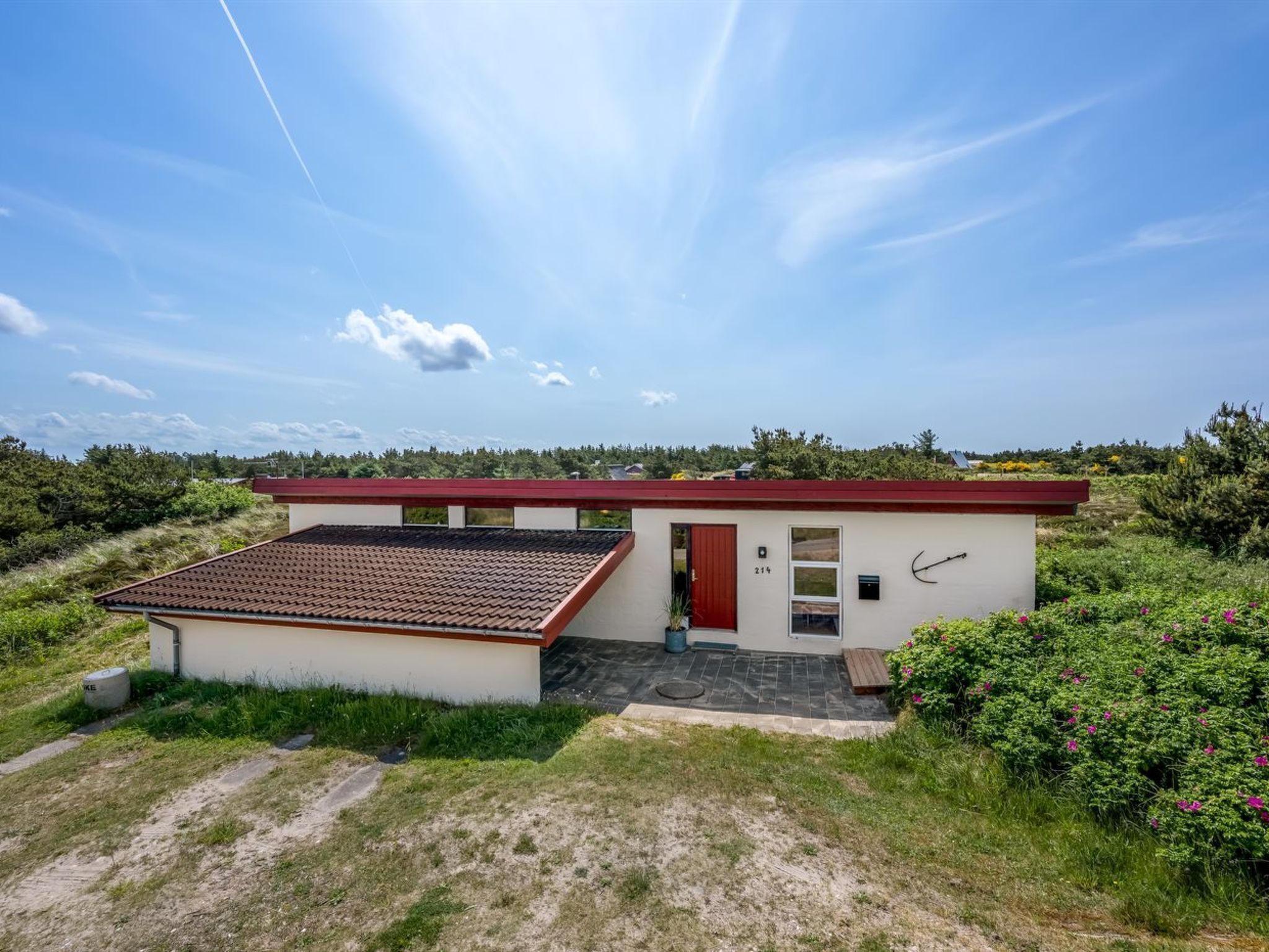 Une maison moderne de plain-pied, avec un toit rouge, un petit porche et une porte portant le numéro 214.