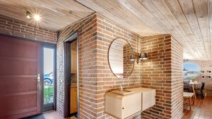 Ein Zimmer mit Backsteinwand, Holzboden, einem runden Spiegel, einem Holzschrank und Blick durch ein Fenster.
