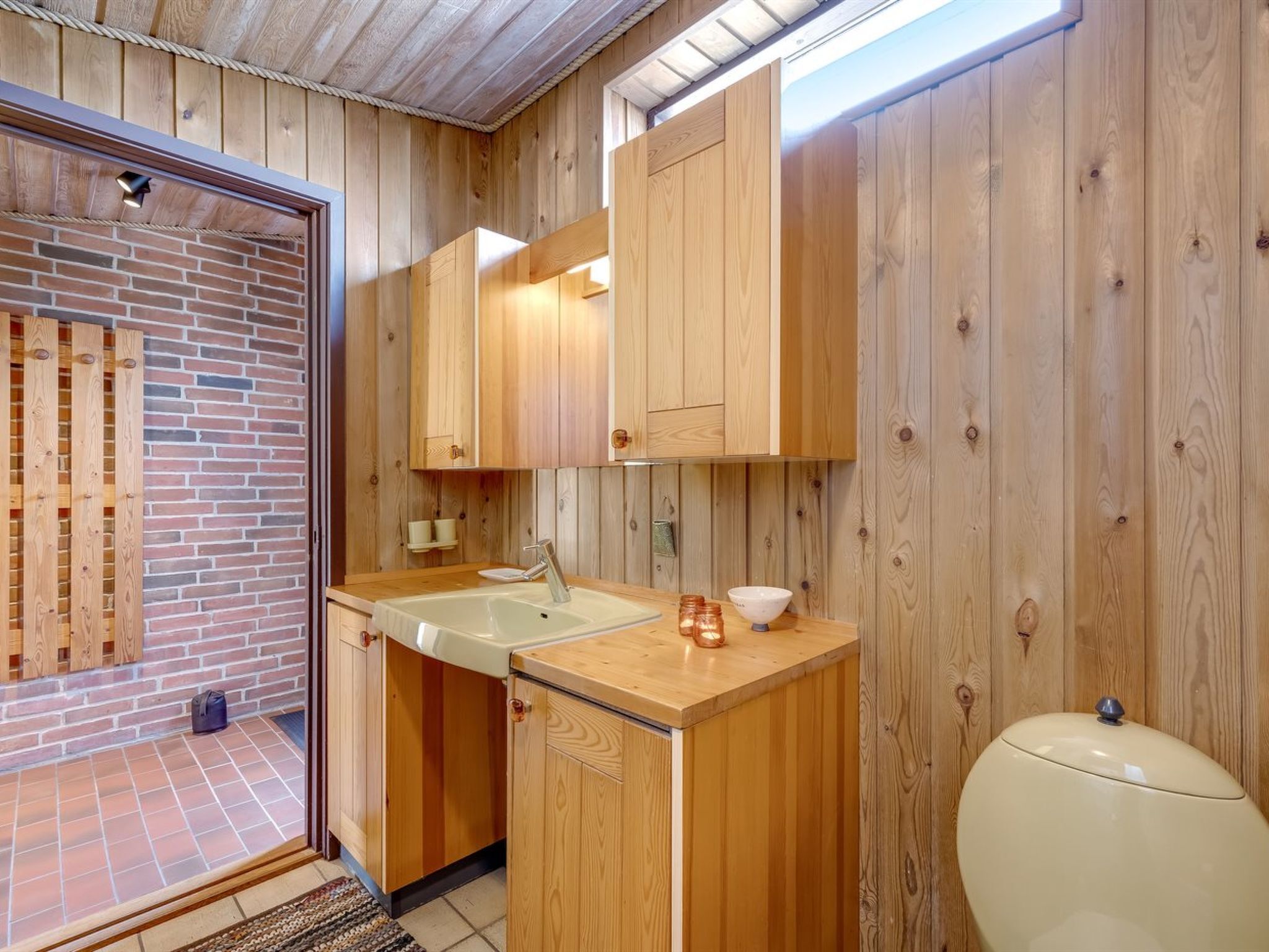 A compact kitchen with wooden cabinets, a sink, and a toilet.