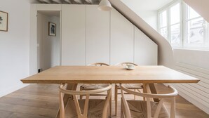 A dining area with a wooden table and chairs, a hanging light fixture, and a view of the outside through a window.