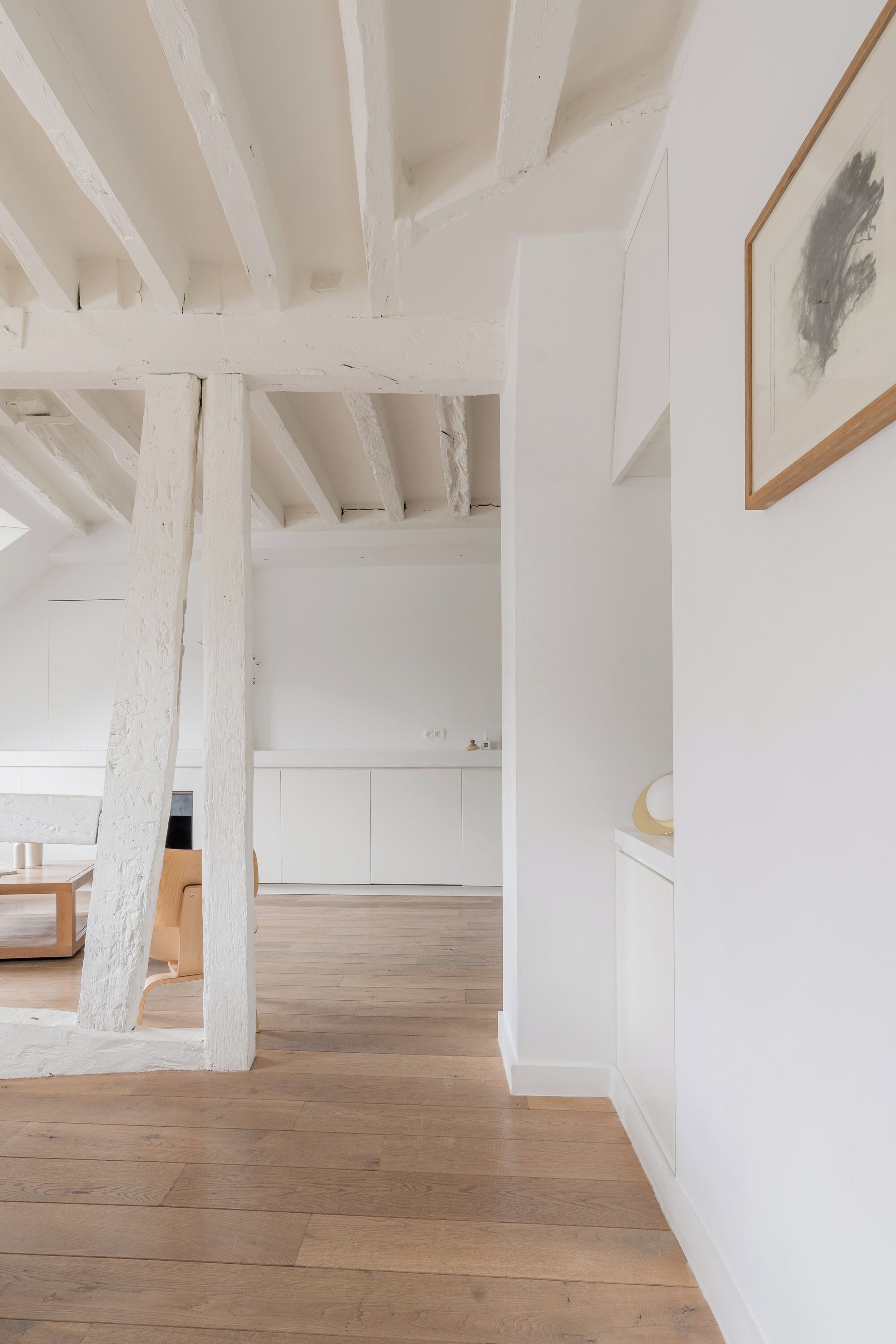 Een ruime kamer met zichtbare houten balken, een houten vloer en witte wanden.