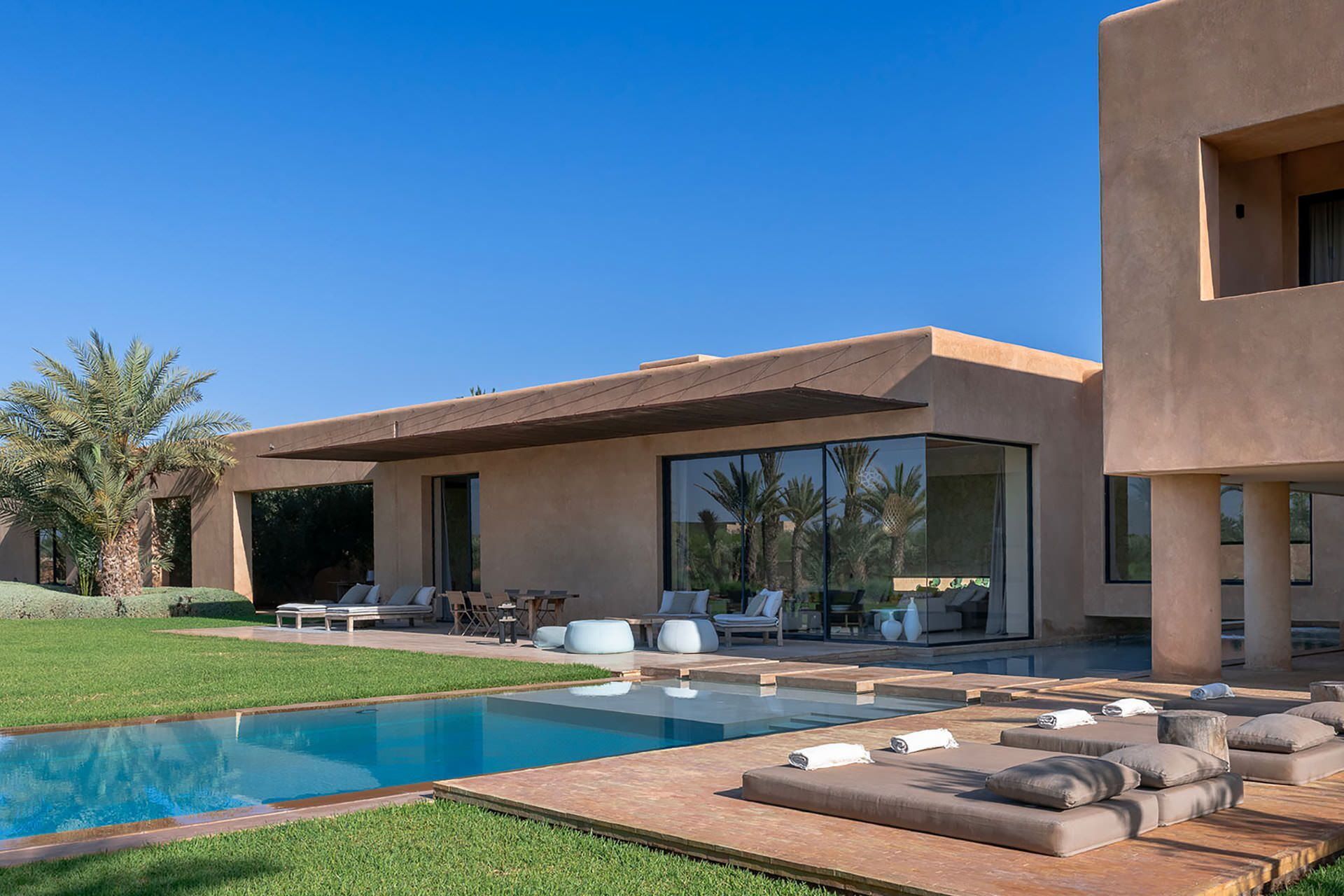 Een modern huis met een zwembad, terras en palmbomen.