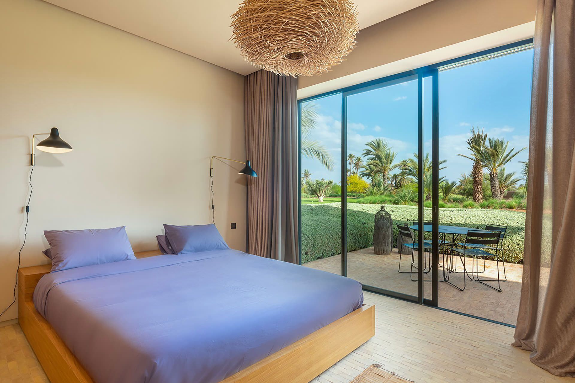 A bedroom with a large bed, a desk, and a view of a garden through a sliding door.