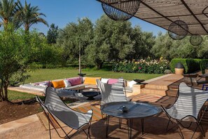Un espace extérieur aménagé en terrasse, avec un ensemble de canapés, des chaises, une table ronde et une pergola décorée de guirlandes lumineuses.