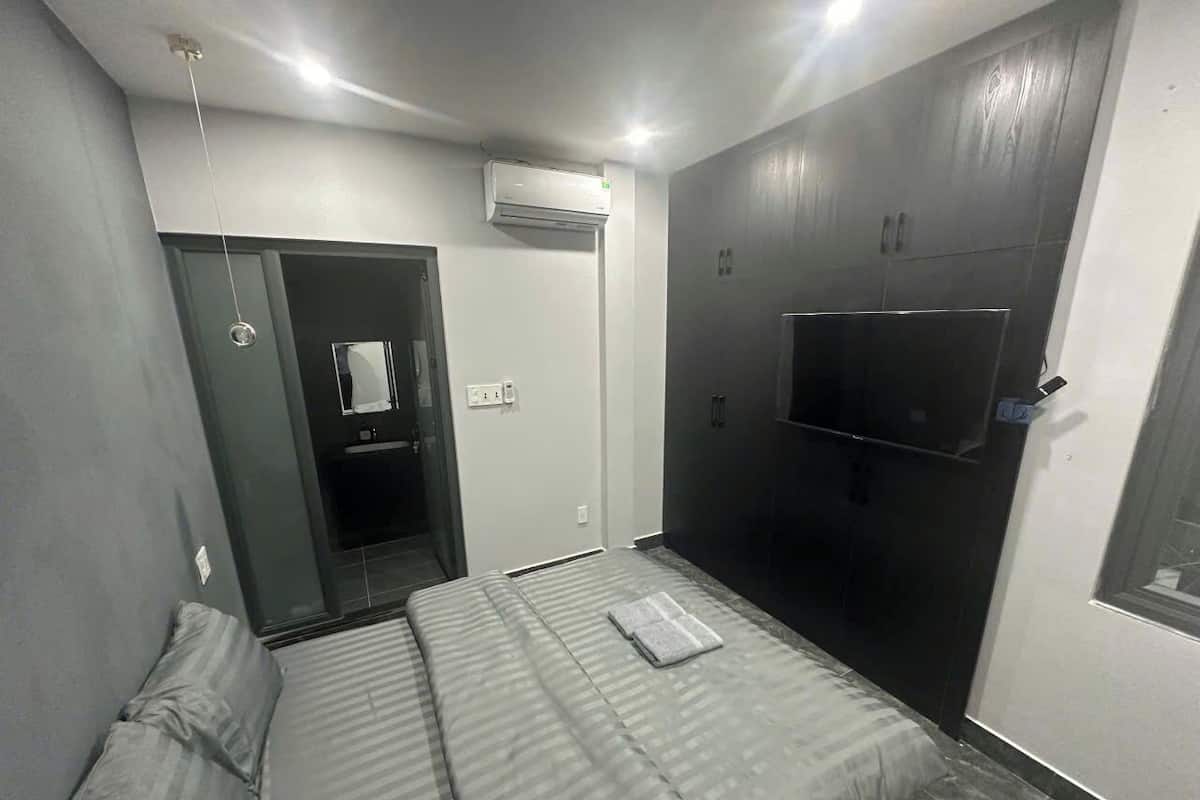 Un dormitorio con una cama, un televisor montado en la pared y una puerta que da al baño.