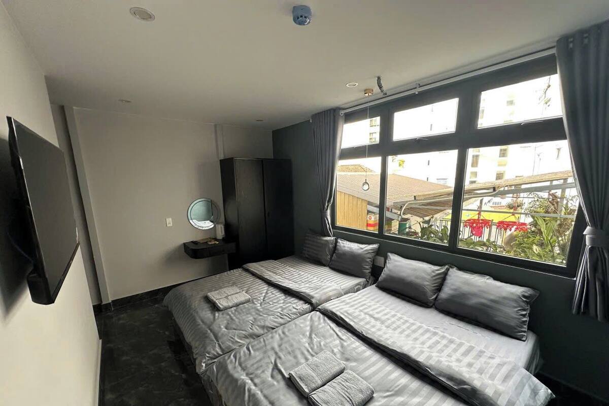 Habitación de hotel con una cama grande, televisión, mesita de noche y ventana con vistas a edificios y zonas verdes.