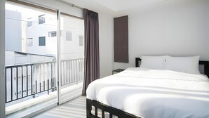 A hotel room with a bed, a nightstand, a window with a view of buildings, and a curtain. - Mitr Inn Mrt Samyot Station - The Grand  (Bangkok)