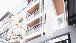 A modern building with a sign for 'Mitr Inn'. It features a large entrance with a black gate, a small outdoor light fixture, and a staircase leading up to the entrance. - Mitr Inn Mrt Samyot Station - The Grand  (Bangkok)
