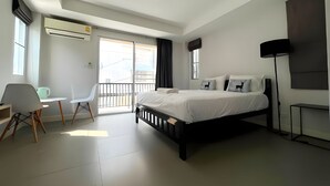 A modern hotel room with a bed, a desk, a chair, a standing lamp, and a view through the balcony doors. - Mitr Inn Mrt Samyot Station - The Grand  (Bangkok)