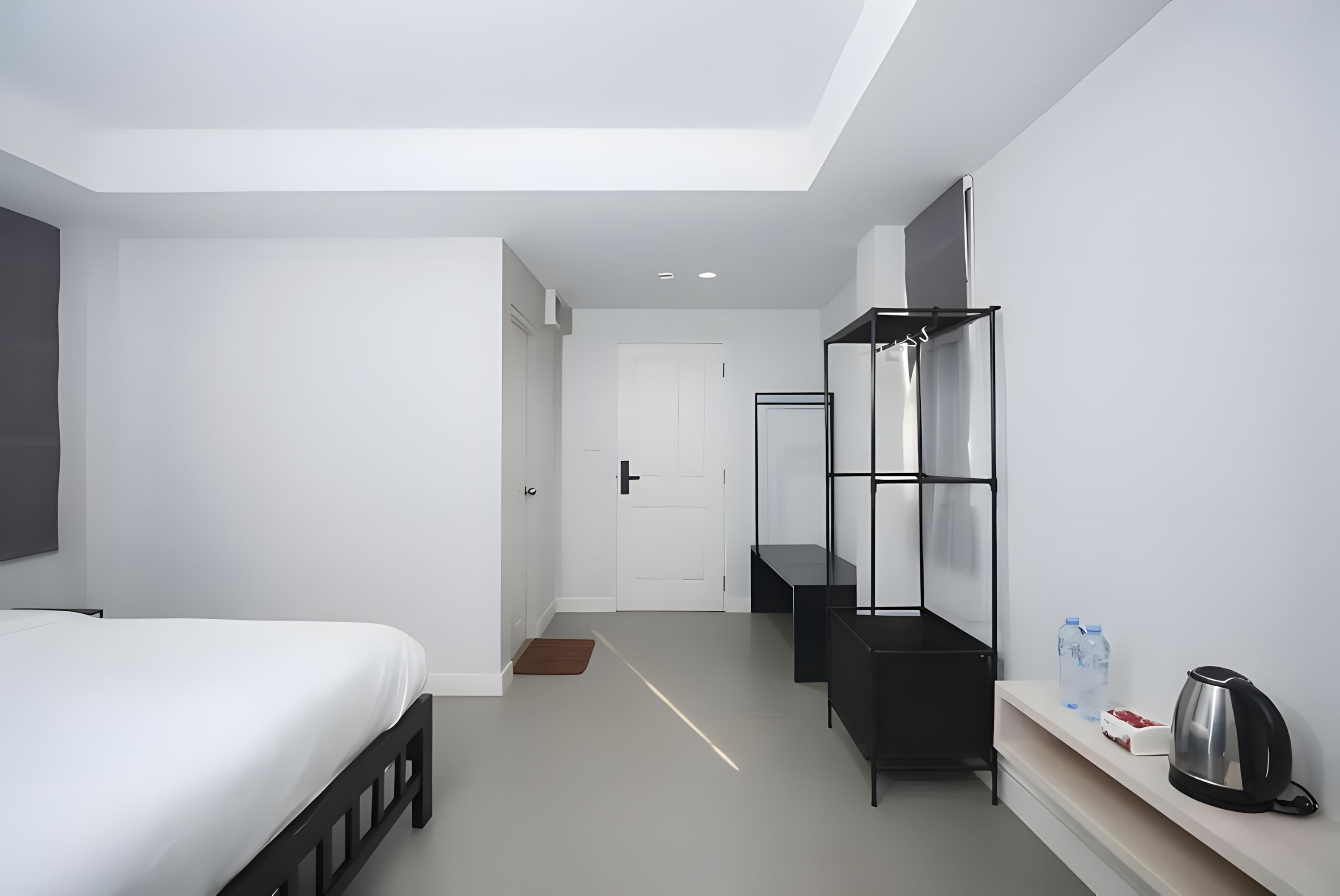 Una habitación de hotel moderna con cama, armario, espejo, repisa con hervidor y jarra de agua.
