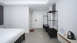 Une chambre d’hôtel moderne équipée d’un lit, d’une armoire, d’un miroir, d’une étagère avec une bouilloire et d’une carafe d’eau.