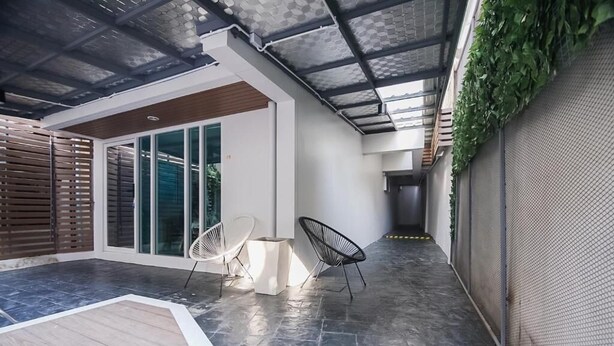 Un patio moderno al aire libre con techo de vidrio, dos sillas blancas y una mesita.