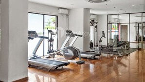 A modern gym with various exercise equipment, large windows, and a polished wooden floor.