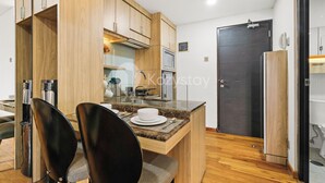 A compact kitchen with wooden cabinets, a built-in microwave, and a small dining area with two chairs.