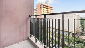 A balcony with a metal railing overlooking a street with buildings and greenery.