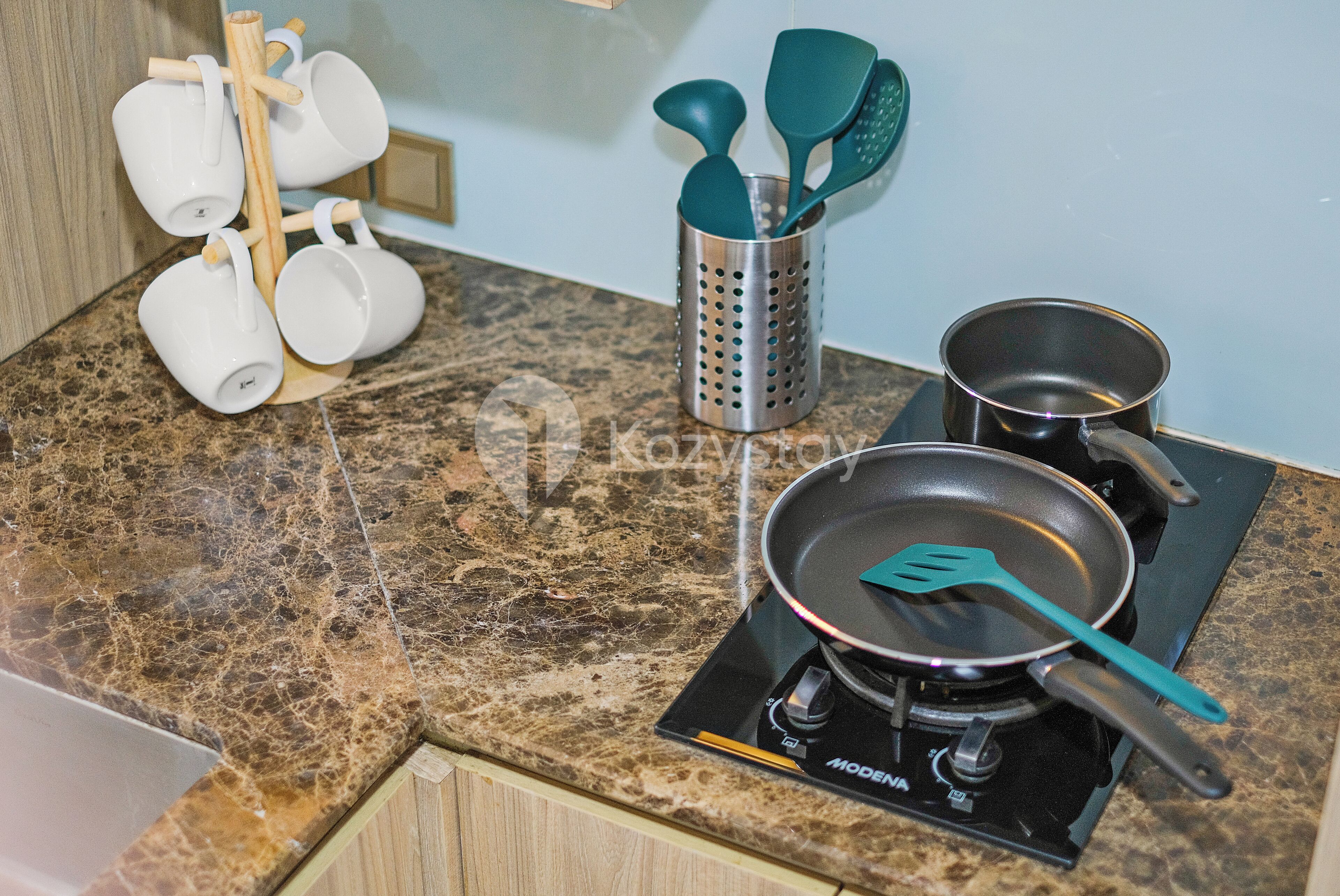 A kitchen with a granite countertop, a stove, a frying pan, and a utensil holder with spatulas.