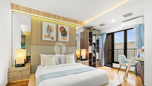 A modern hotel room with a large bed, wooden flooring, a balcony with blue curtains, and artwork on the wall.