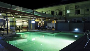 A swimming pool with a tiled deck and a covered area with seating. - Network Hotel and Suites (Ilesa)