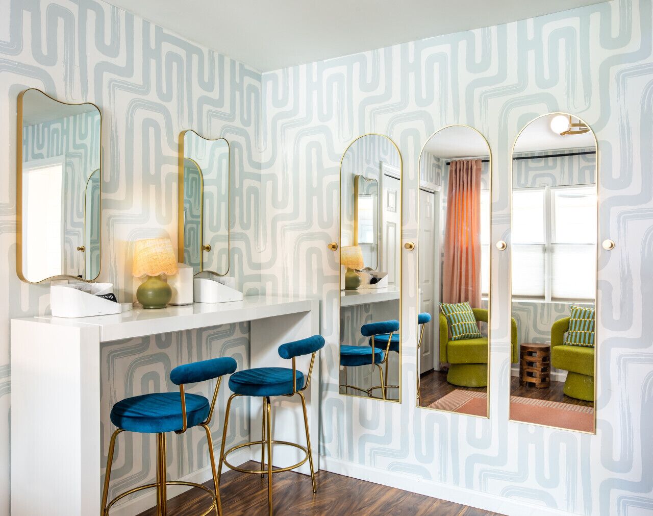 Ein Badezimmer mit einem weißen Waschtisch, drei blauen Barhocker und Wänden mit Spiegeln und einem geometrischen Muster.