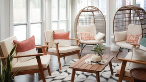 A modern living room with a large window, wicker chairs, a wooden coffee table, and a potted plant. - Savannah Retreat|Htd Pool|Pickleball|Hot tb|Golf (Savannah)