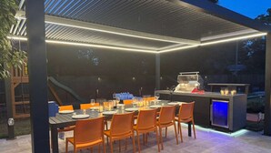 An outdoor patio with a table set for dining, a grill, and ambient lighting. - Savannah Retreat|Htd Pool|Pickleball|Hot tb|Golf (Savannah)