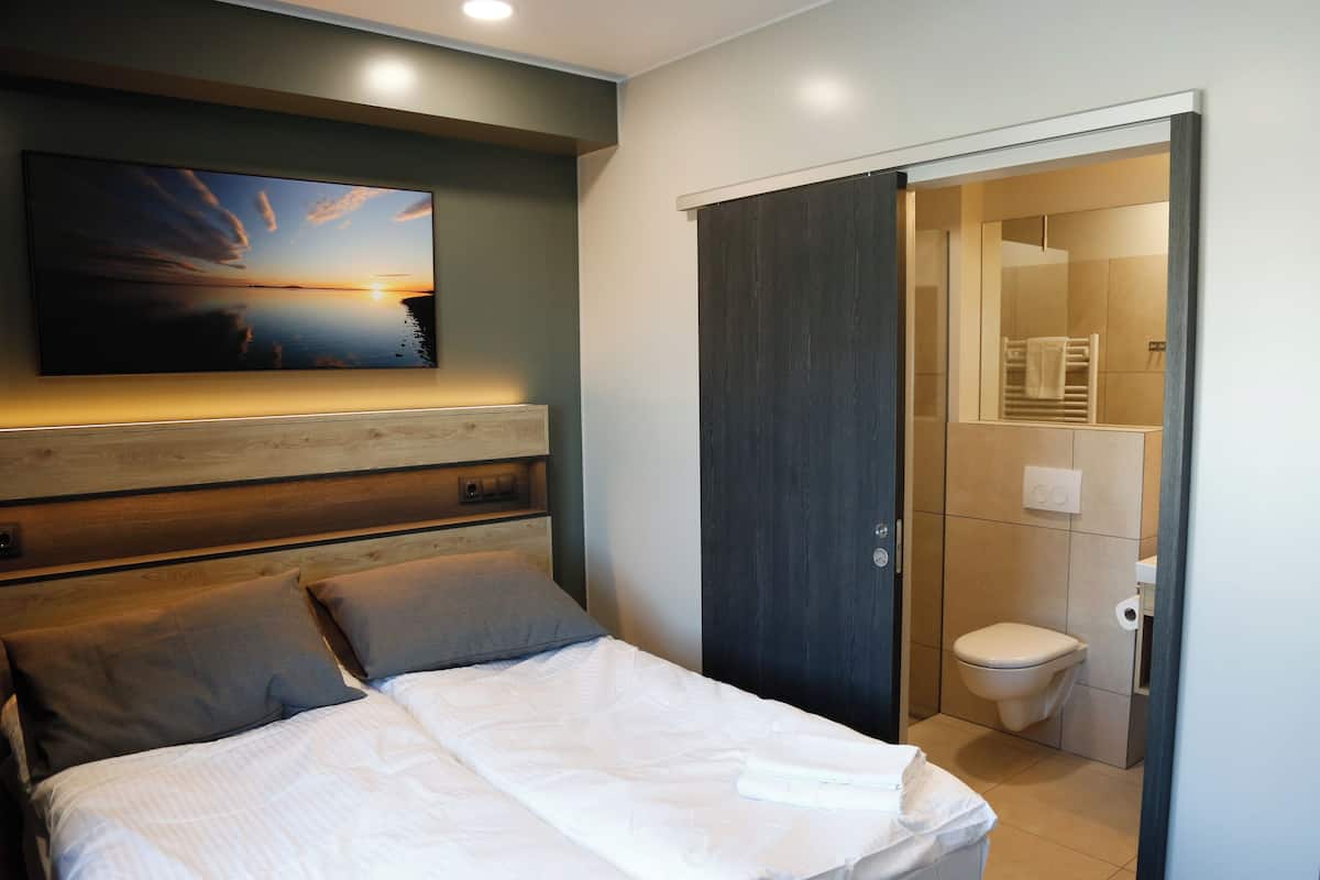 A bedroom with a bed, a headboard, a wall-mounted TV, and a door leading to a bathroom.
