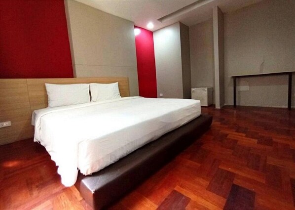 Une chambre d’hôtel avec un lit, un plancher en bois et un mur d’accent rouge.