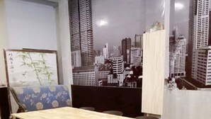 Ein Essbereich mit einem Holztisch, schwarzen Stühlen, einem blauen Sofa und einem Wandgemälde mit Stadtansicht.
