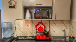 A compact kitchen with a microwave, kettle, and dish rack.