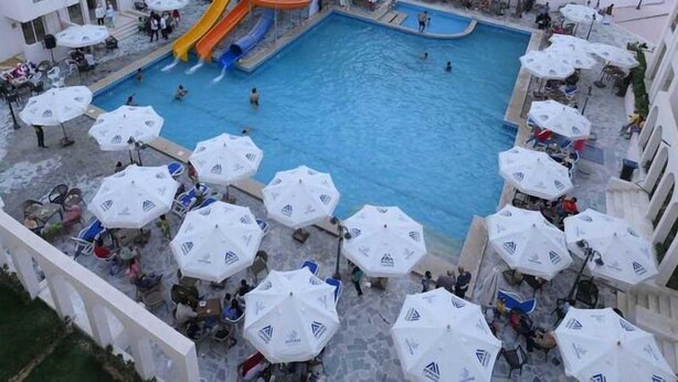 A multi-level pool area with a central water slide, surrounded by multiple balconies and outdoor seating areas with umbrellas.