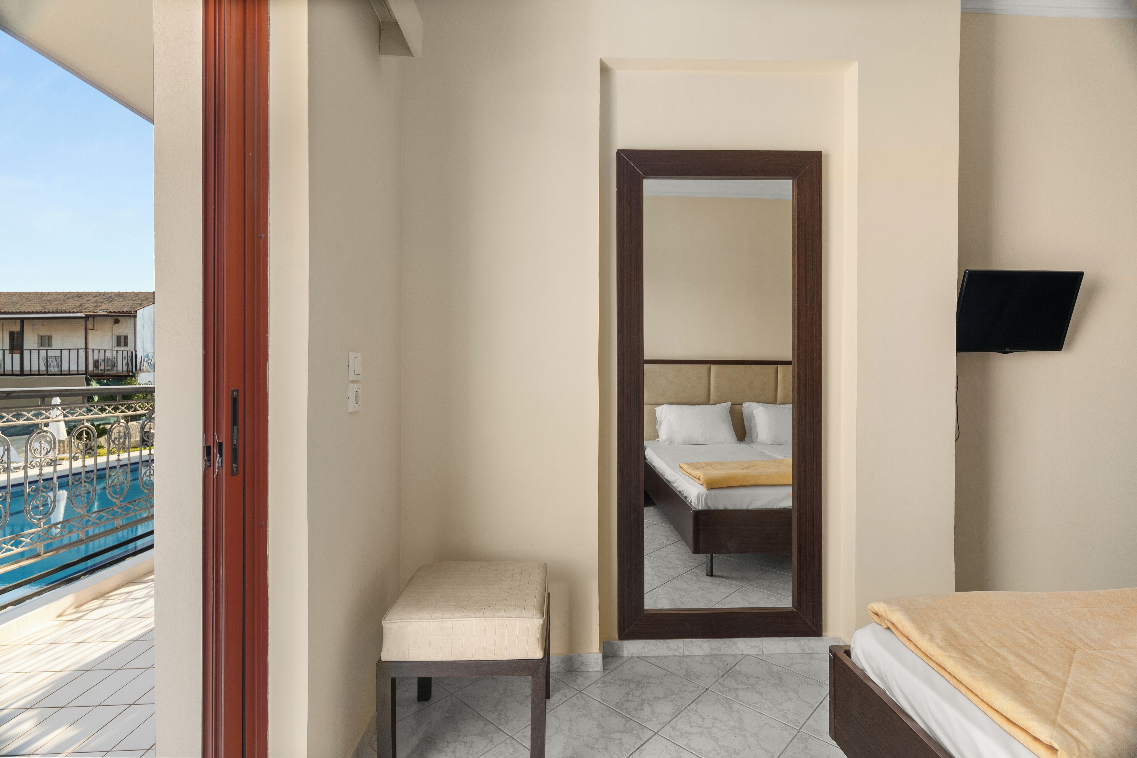 A hotel room with a bed, a small stool, a TV, and a bathroom mirror.