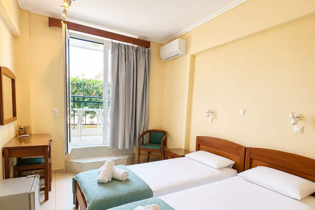 A hotel room with two beds, a desk, a chair, and a window with curtains.