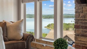 Quarto com uma grande janela com vista para um lago, um sofá de couro marrom e uma parede de tijolos.