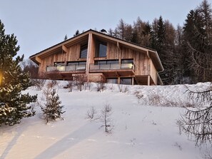 Une cabane en bois dotée d’un balcon, entourée de neige et d’arbres.