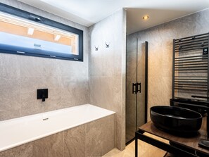 A modern bathroom with a large white bathtub, a glass shower enclosure, and a black basin on a wooden table.