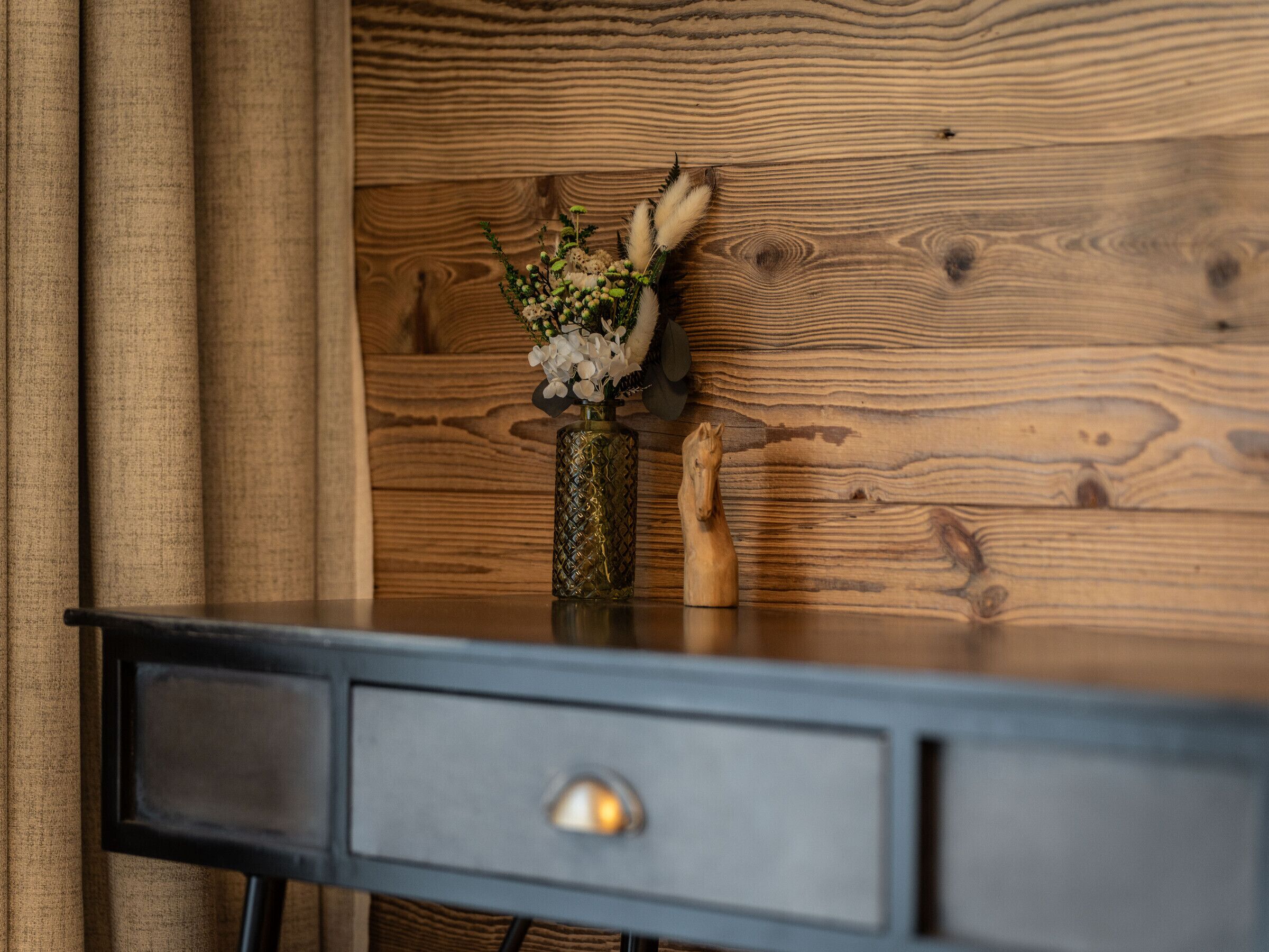 A wooden wall with a vase of flowers and a wooden horse figurine on a desk.