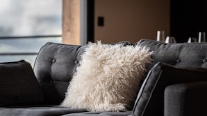 A dark grey sofa with a fluffy white pillow and a grey throw blanket.