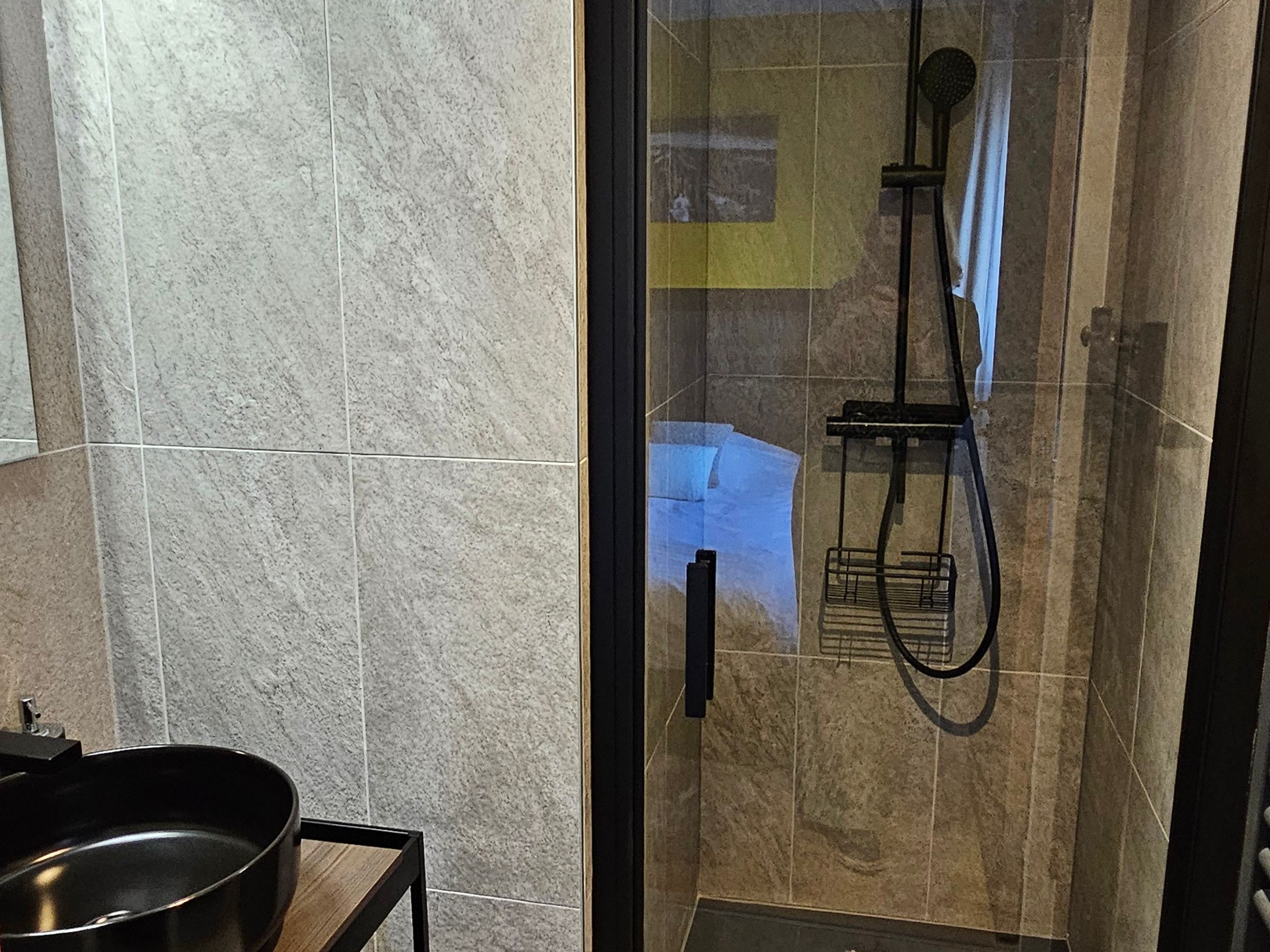 A modern bathroom with a glass-enclosed shower, a black sink, and a tiled wall.