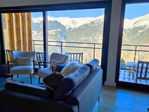 Habitación con un ventanal grande que da a montañas cubiertas de nieve. Hay un sofá y dos sillones con cojines.
