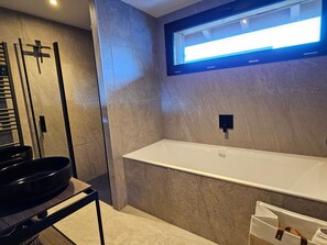 Une salle de bain moderne avec une grande baignoire blanche, un robinet noir et un miroir fixé au mur.