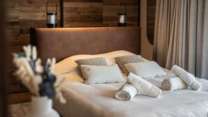 A modern bedroom with a wooden headboard, two bedside lamps, and a neatly made bed with rolled towels.