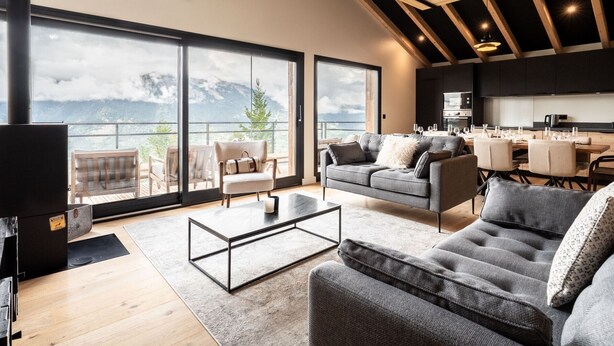 A modern living room with a large sliding glass door leading to a balcony with mountain views.