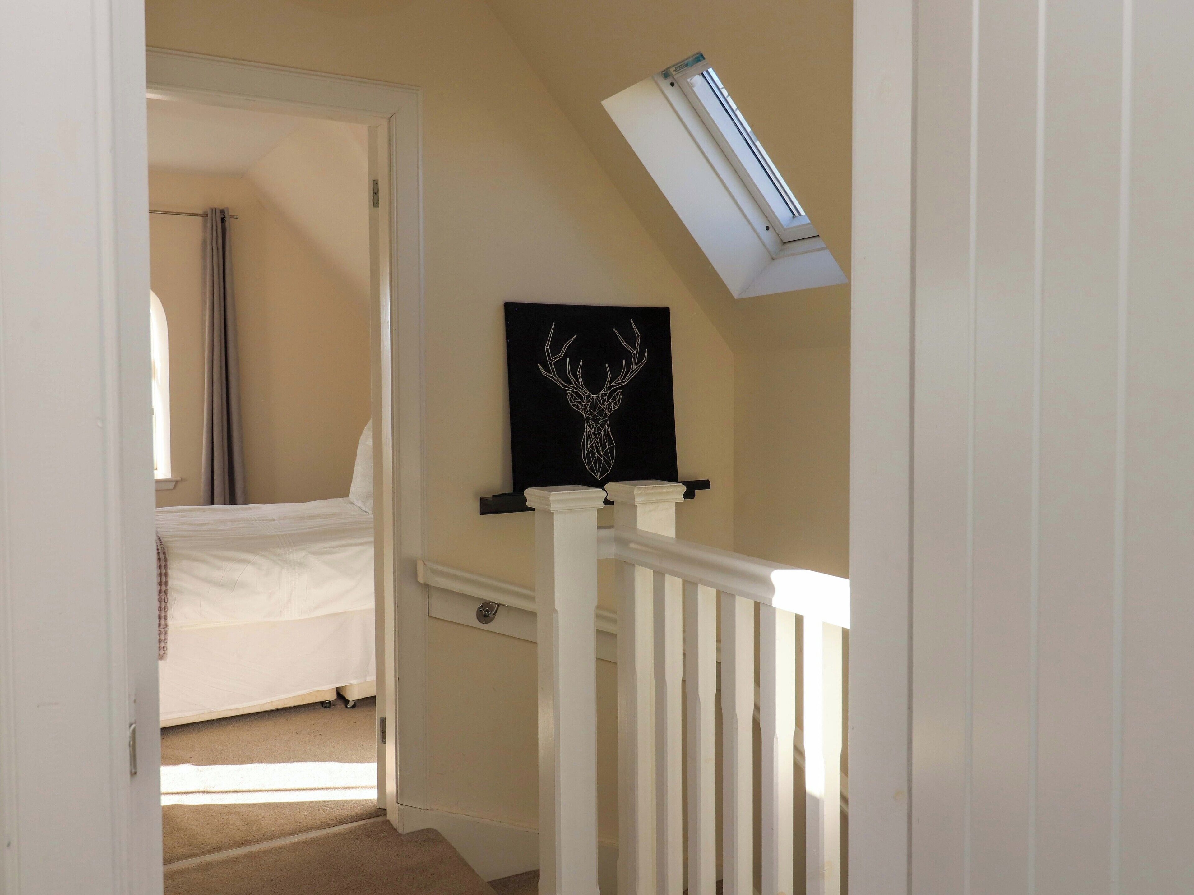 Ein schmaler Flur mit einem Bett im Hintergrund, einer schwarzen Kunst mit einem Hirschkopf und einem Oberlicht.