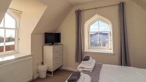 A bedroom with a bed, a dresser, a television, a window with curtains, and a radiator. - View Cottage (Inverness)
