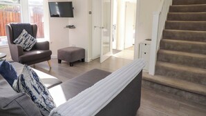 A living room with a sofa, ottoman, and a TV mounted on the wall. - View Cottage (Inverness)