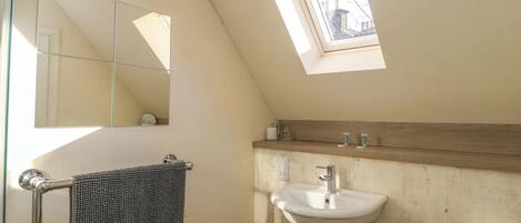 A bathroom with a skylight, a towel rack, a sink, and a toilet.