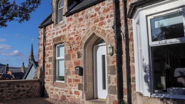 A stone building with a white door, a window with a black frame, and a small balcony. - View Cottage (Inverness)