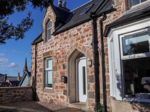 A stone building with a white door, a window with a black frame, and a small balcony. - View Cottage (Inverness)