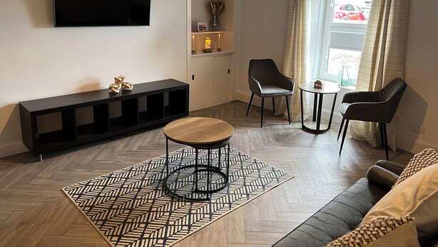 A modern living room with a flat-screen TV, a black console table, a round coffee table, two armchairs, and a small side table. - 1 Links Place (Nairn)