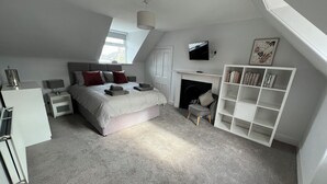 A bedroom with a bed, nightstands, a TV, a fireplace, and a bookshelf. - 1 Links Place (Nairn)